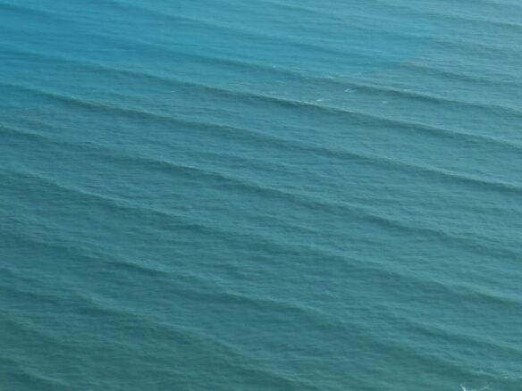 Large swell waves arriving on a coastline during a sunny day with clear